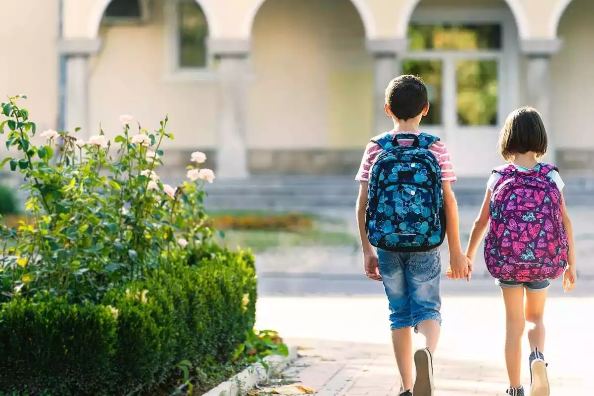 dos niños con mochila caminan hacia la escuela
