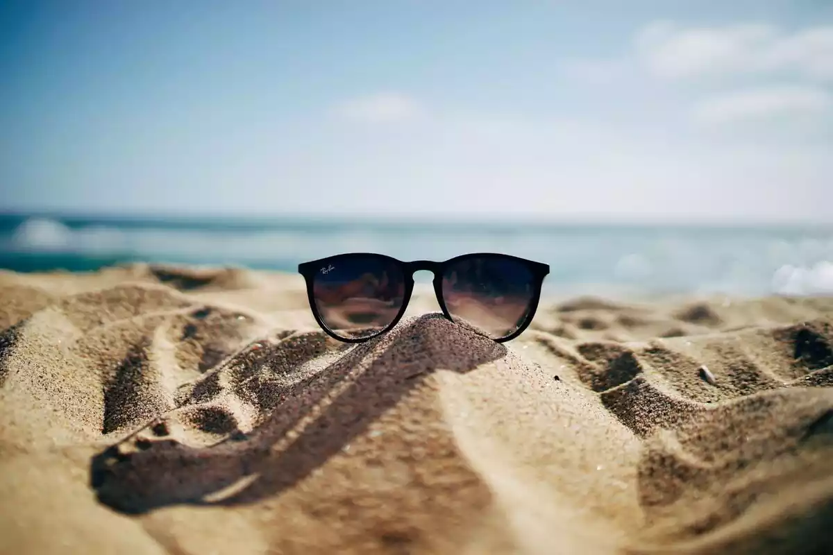 Gafas de sol encima de la arena con el mar de fondo