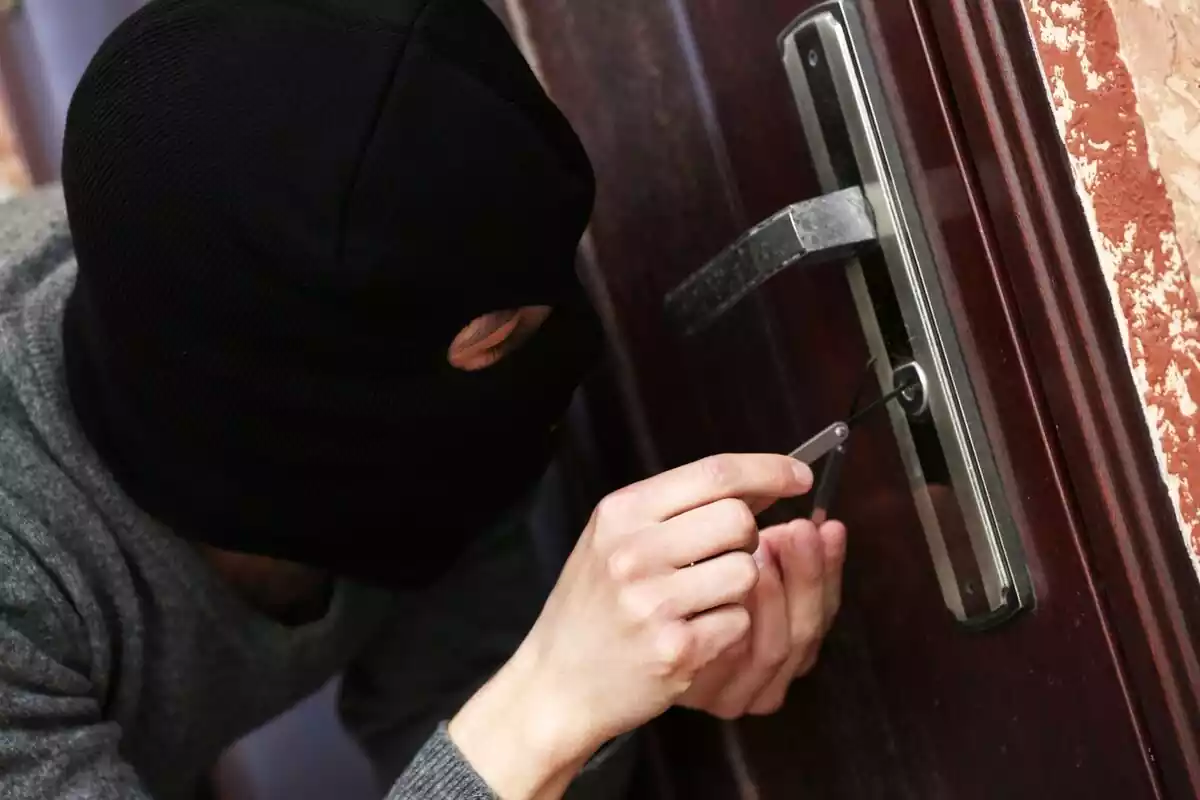 Ladrón con pasamontañas intentando forzar la puerta de una casa