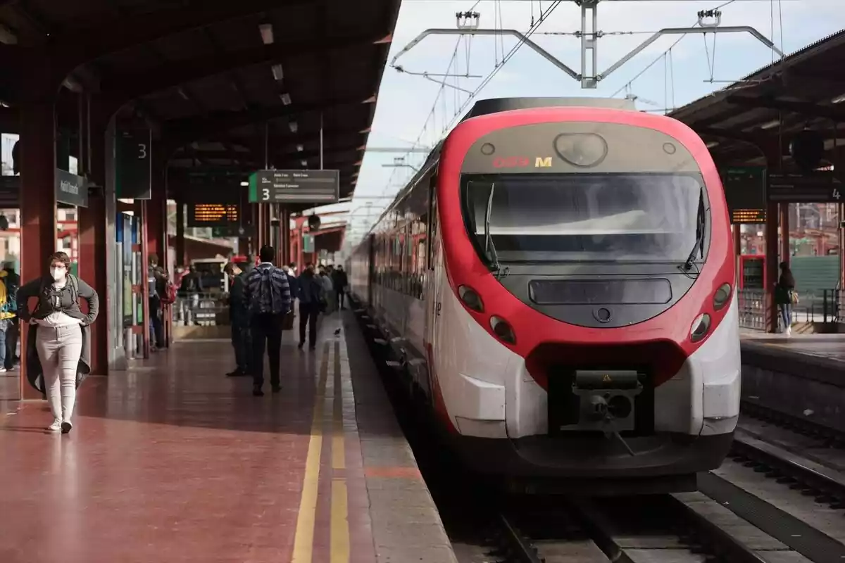 Un tren de cercanías rojo parado en la estación con el andén lleno de viajeros