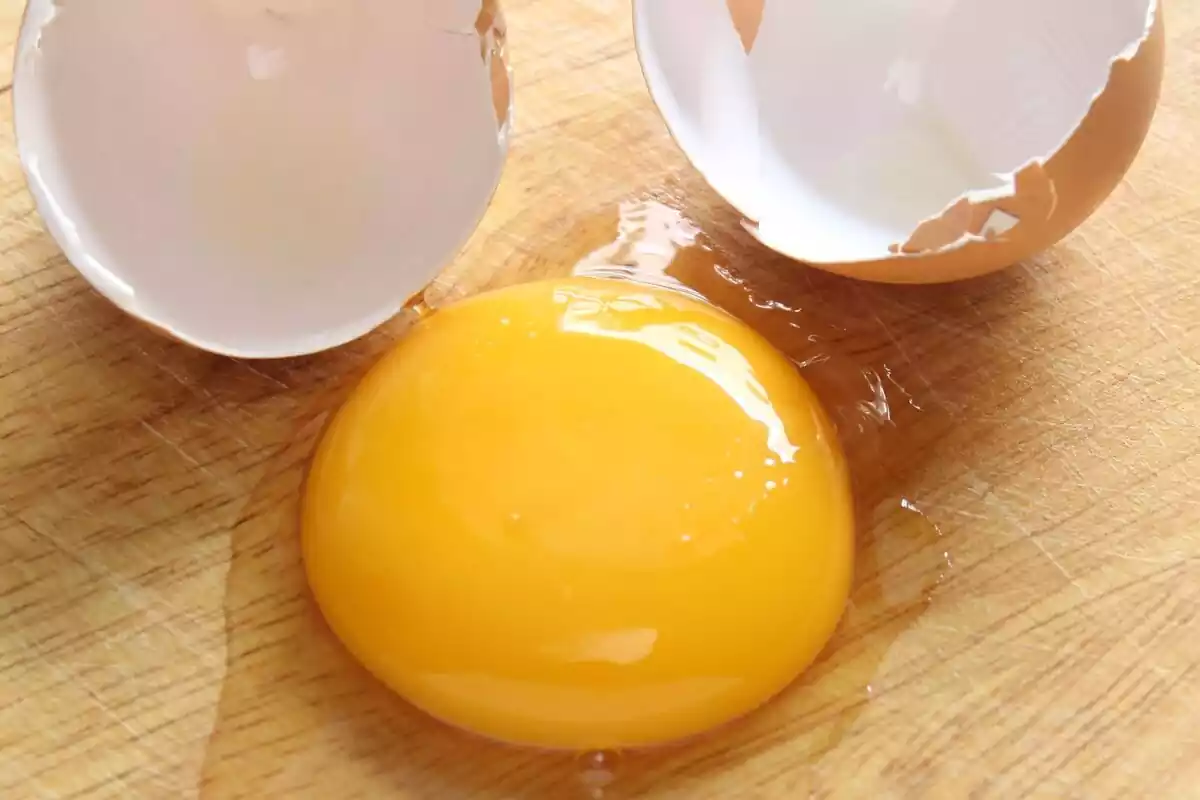 Un huevo con su yema amarilla y la clara encima sobre una tabla de madera