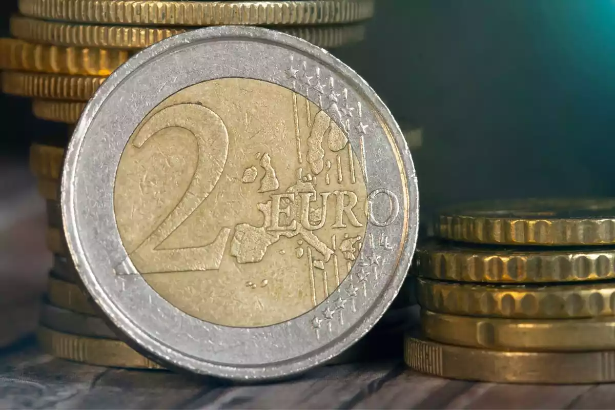 Una moneda de dos euros junto a otras monedas de euros apiladas