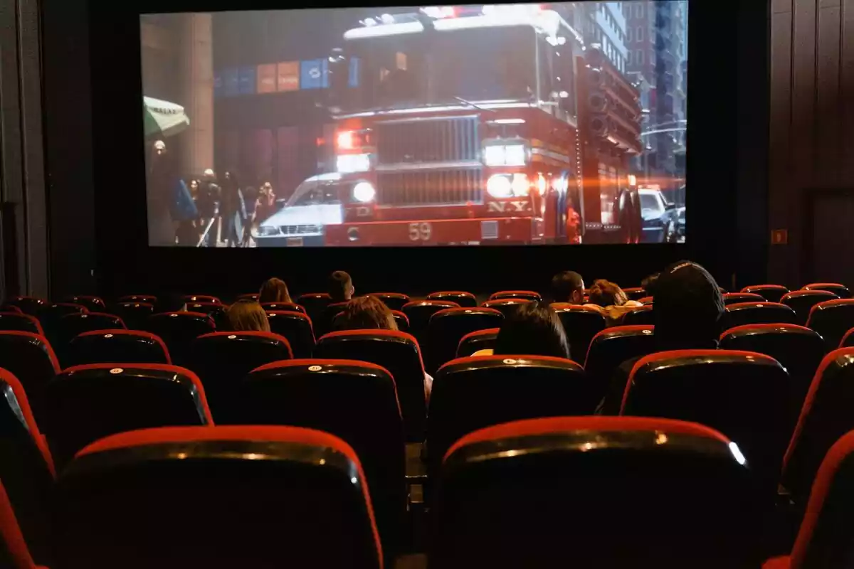 Una sala de cine con muchas butacas rojas vacías y un película en proyección