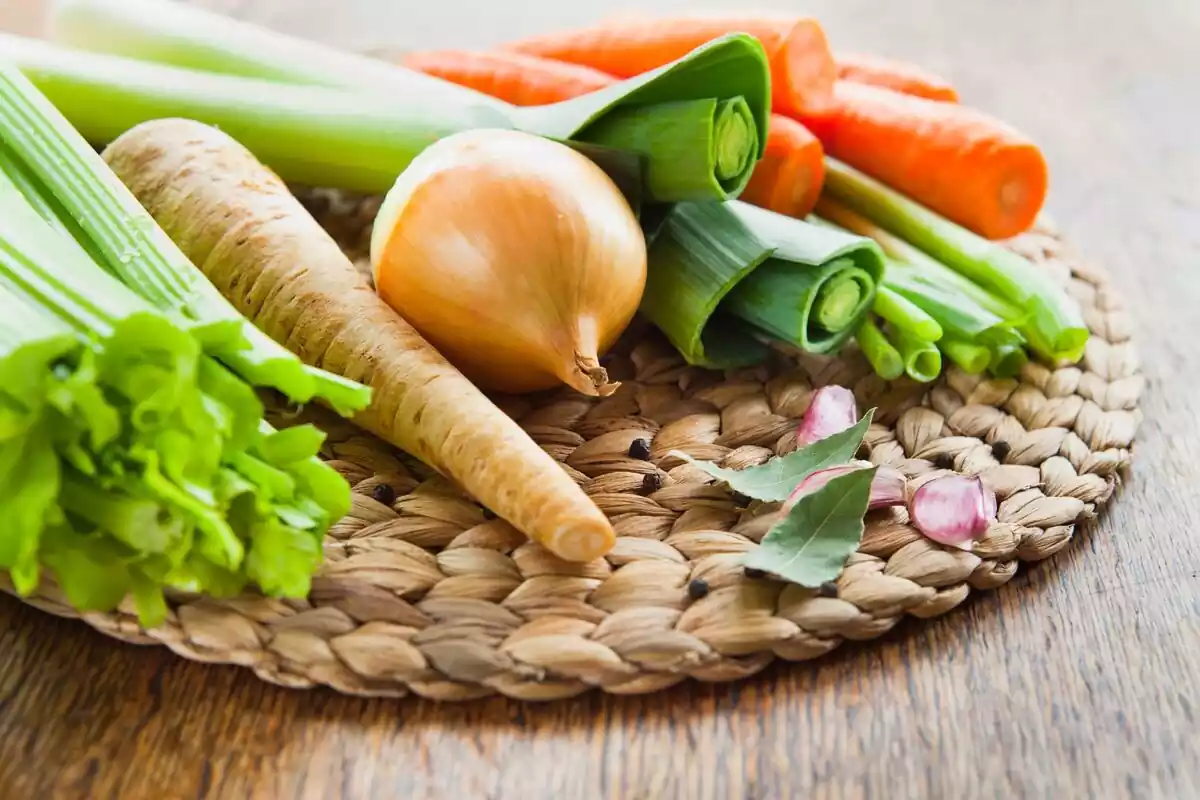 Diferentes verduras apoyadas en un mimbre: ajo, cebolla, zanahoria, apio...