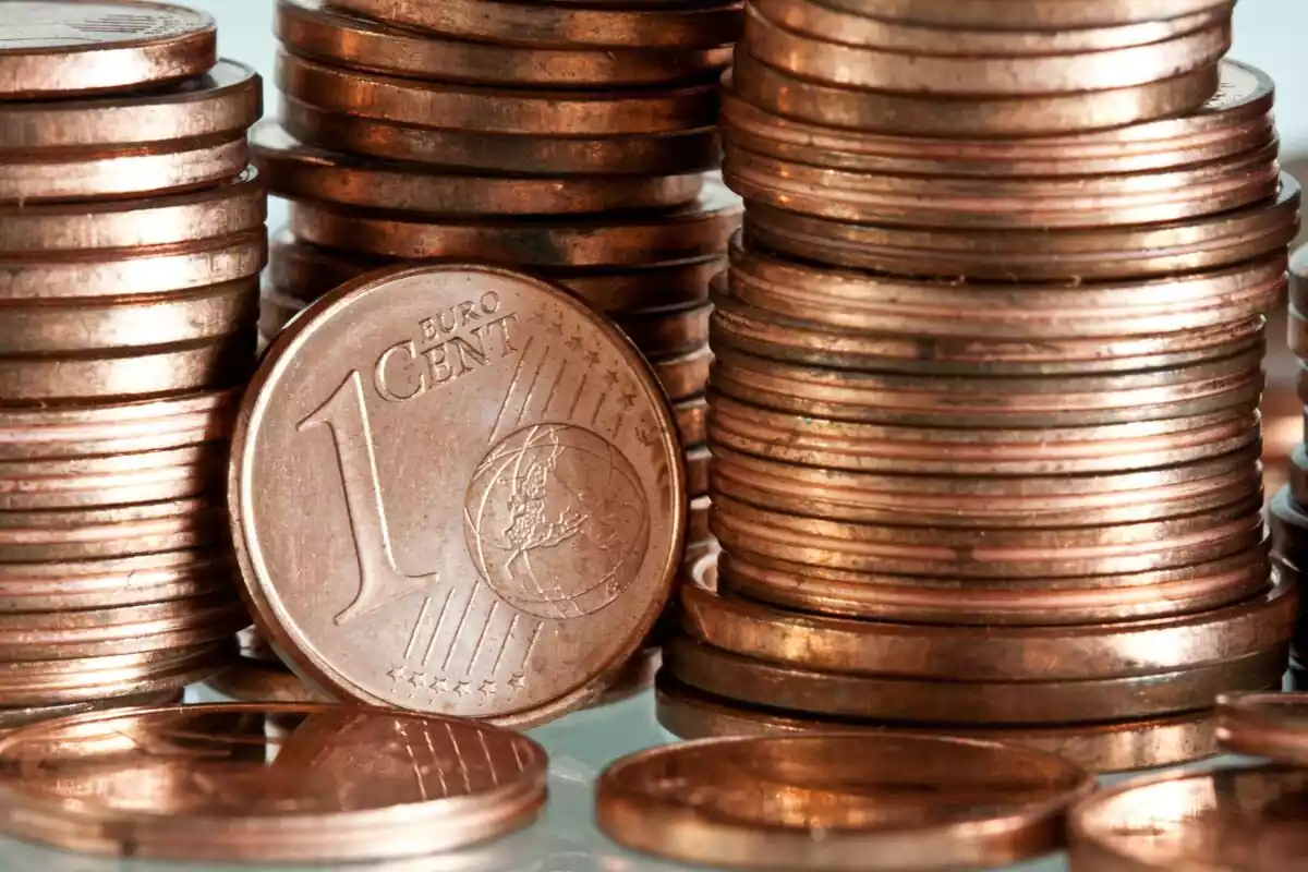 Montones de monedas de céntimos de euro y una moneda de 1 céntimo en primer plano