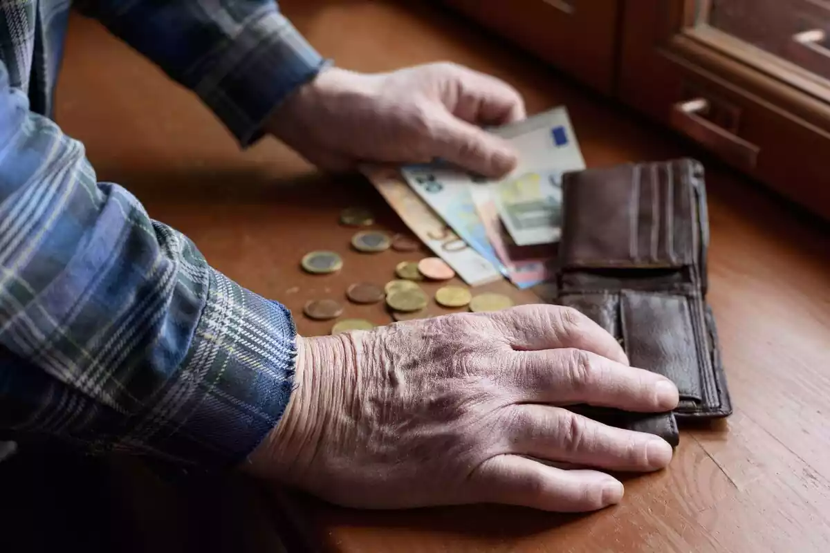 Un hombre contando dinero con la cartera vacía junto a billetes y monedas