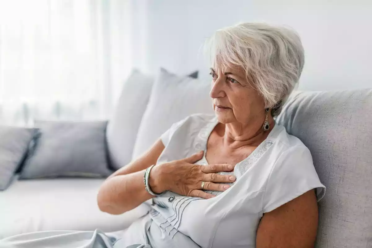 Una mujer mayor sentada en el sofá con la mano en el pecho