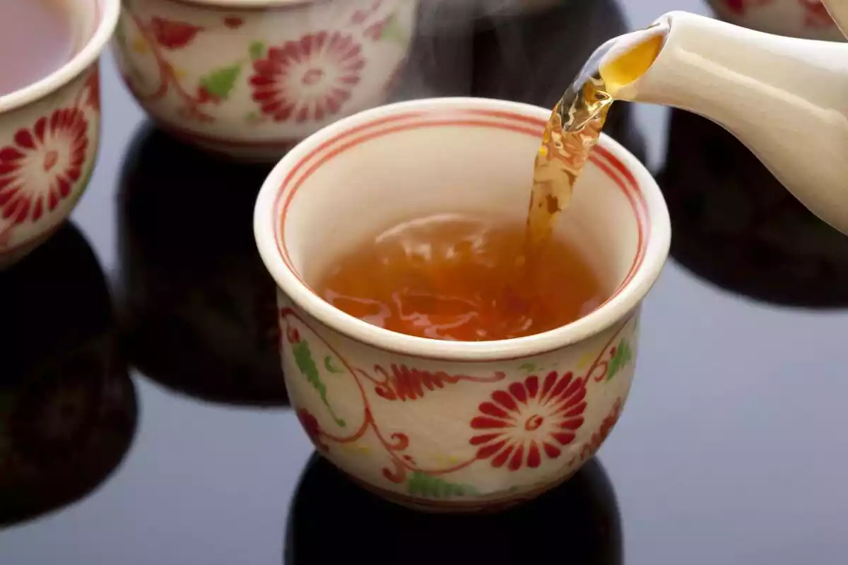 Una taza de té siendo rellenada con la bebida de color naranja