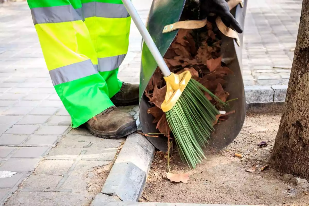 Un barrendero con su escoba, recogiendo unas hojas en la calle