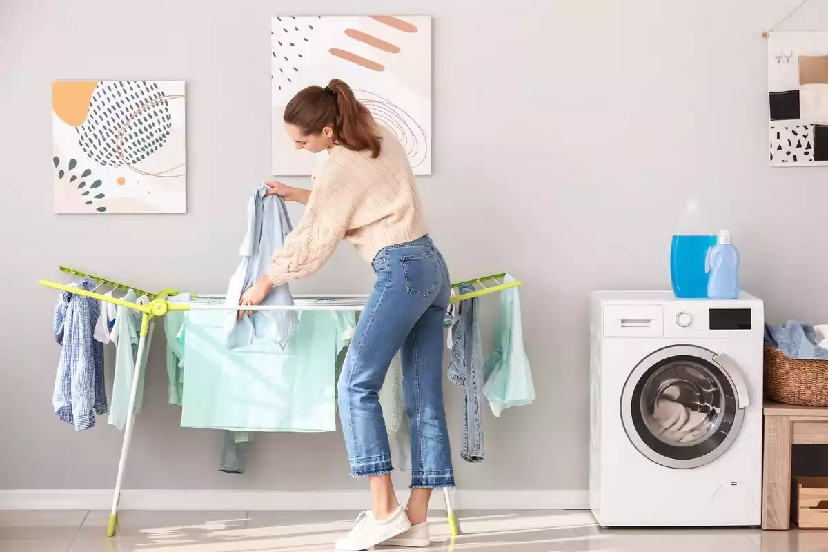 Una mujer colgando la ropa en su casa junto a una lavadora