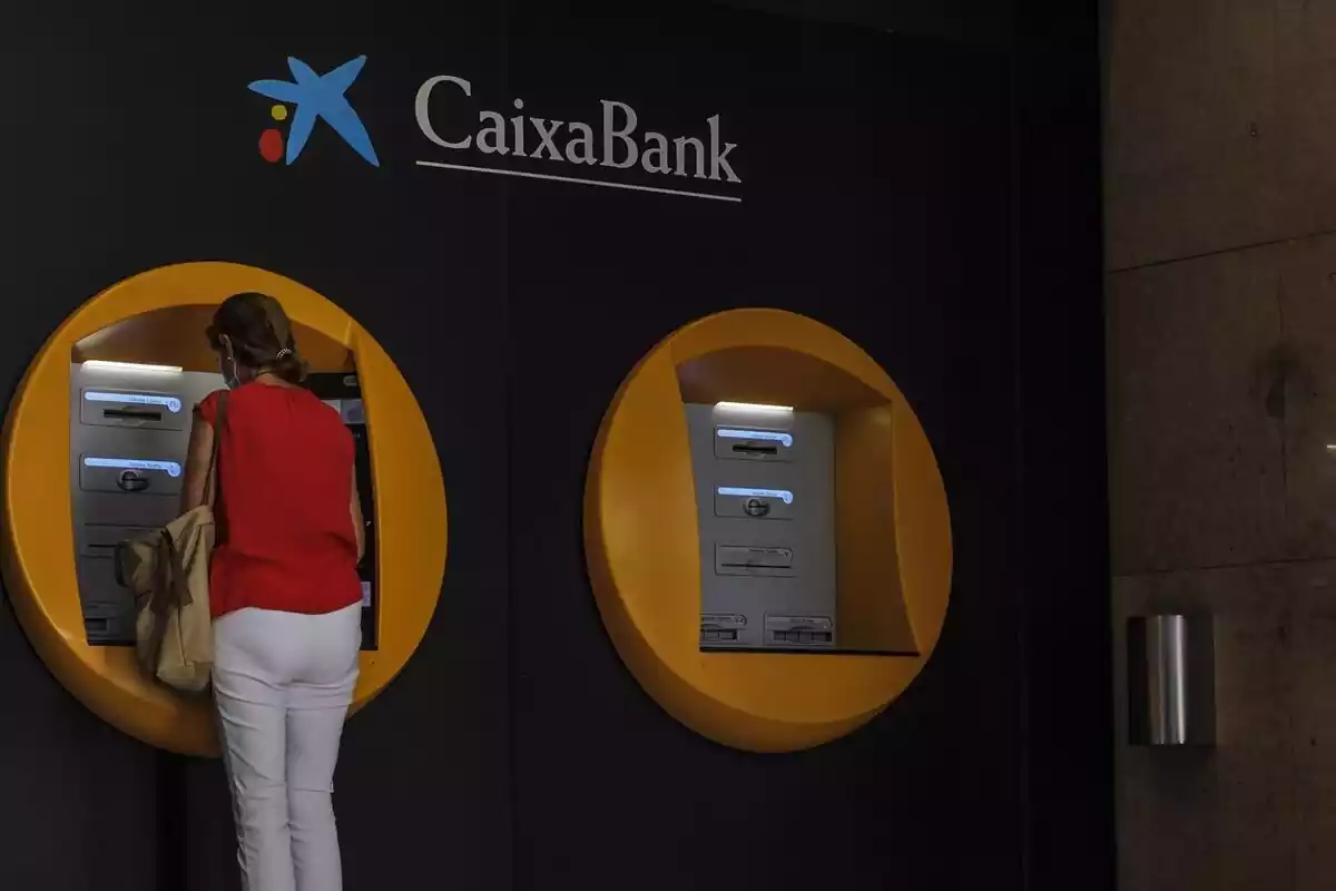 Una mujer sacando dinero del cajero amarillo de CaixaBank