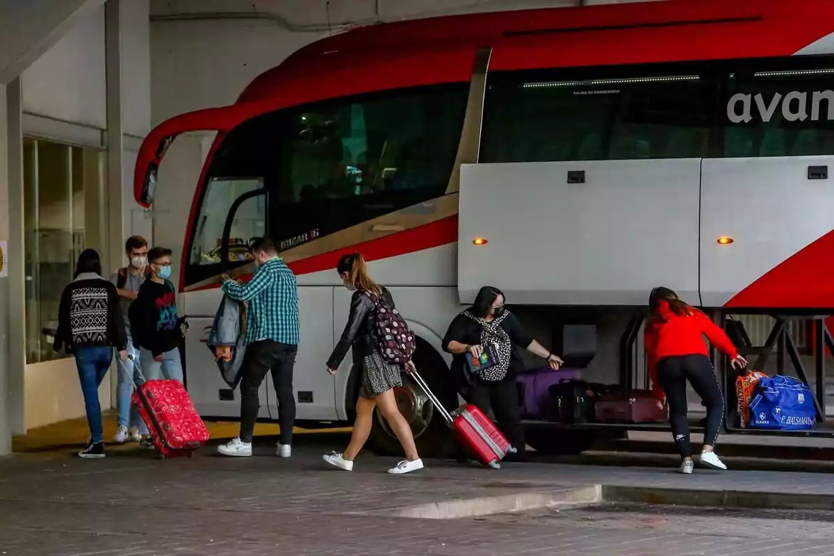 Varios viajeros recogiendo sus pertenencias de un autobús rojo