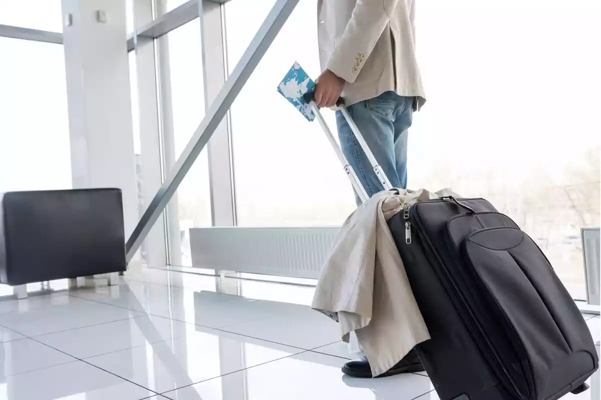 Hombre con equipaje de mano en un aeropuerto, con el billete de avión en la mano