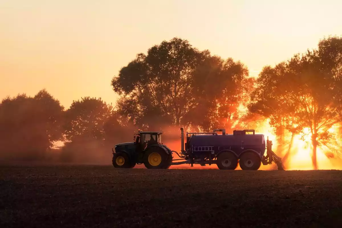 Imágen de un agricultor trabajando sus tierras con la ayuda de un tractor y un remolque