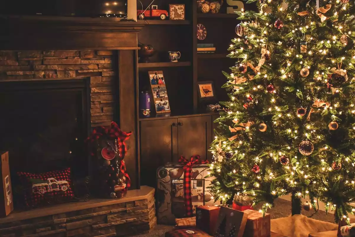 Imágen de una casa decorada con adornos navideños y un árbol con luces y regalos debajo