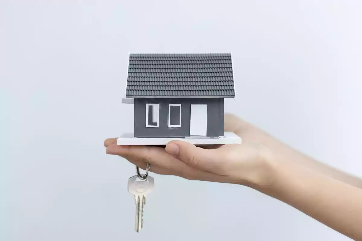 Imágen de una maquetación de una vivienda en las manos de una persona con las llaves de una casa