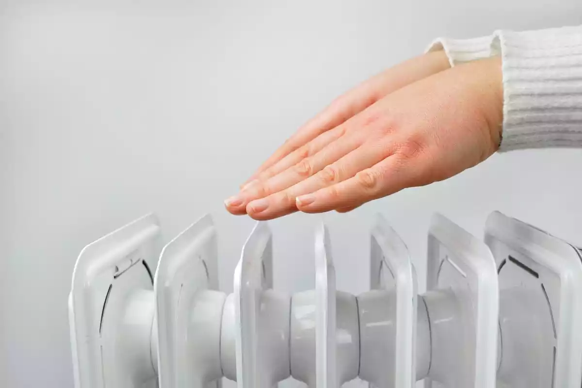 Imágen de una mujer poniendo las manos encima de un radiador de calefacción eléctrica