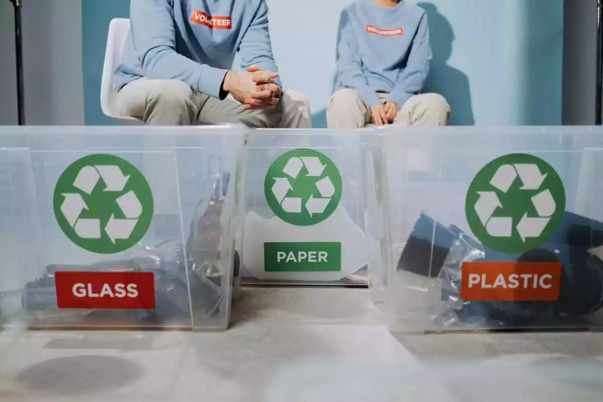 Imágen de unos contenedores de plástico con el símbolo de reciclar y materiales para reciclar en ellos