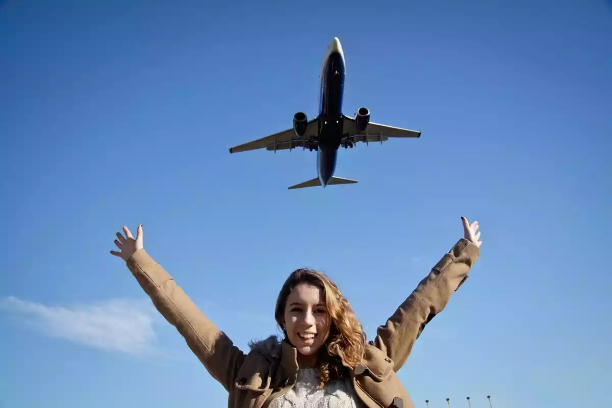 Mujer con los brazos levantados debajo de un avión que sobrevuela el cielo