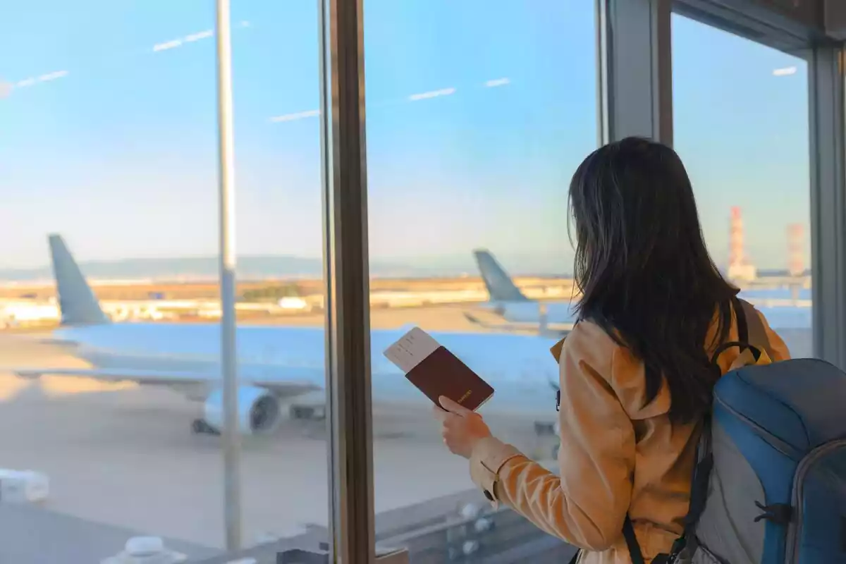 Mujer con un pasaporte en la mano mirando desde de la aeropuerto un avión parado en la pista
