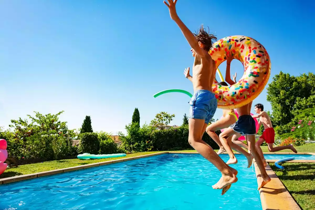 Niños saltando con flotadores a una piscina en verano