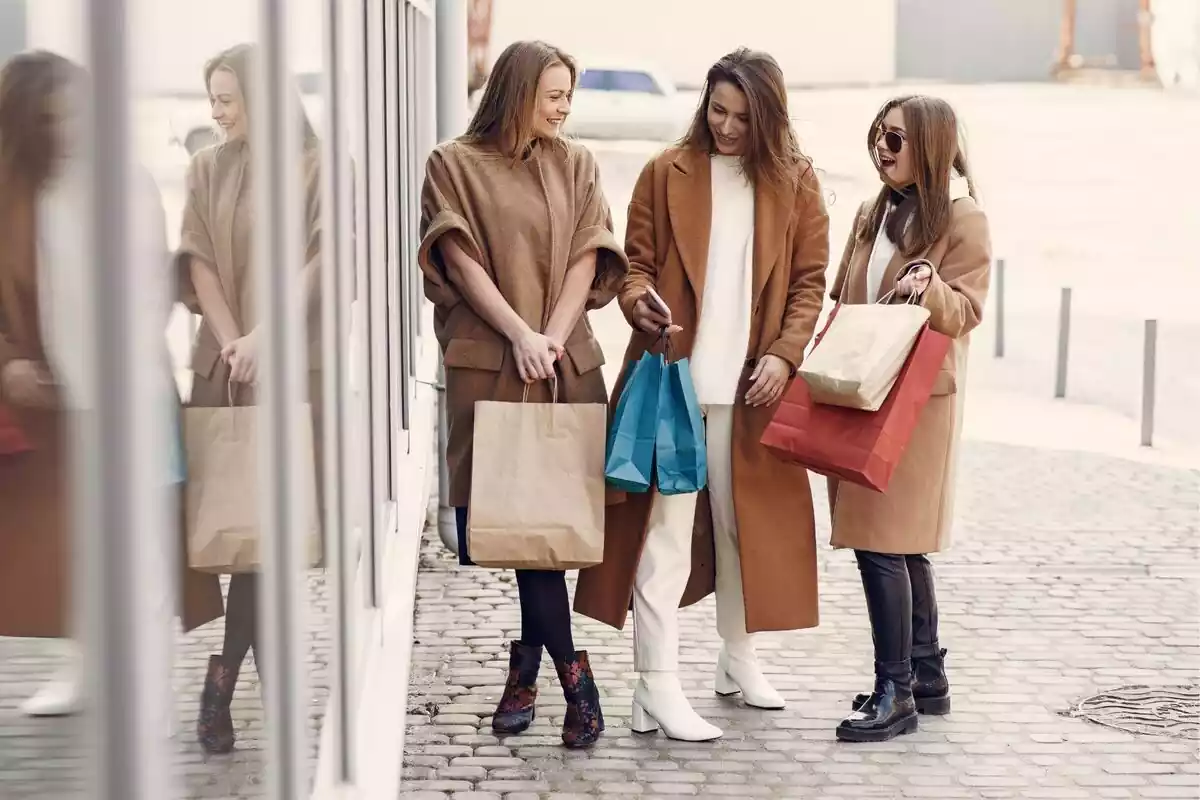 Tres mujeres abrigadas a las afueras de un centro comercial con bolsas con compras