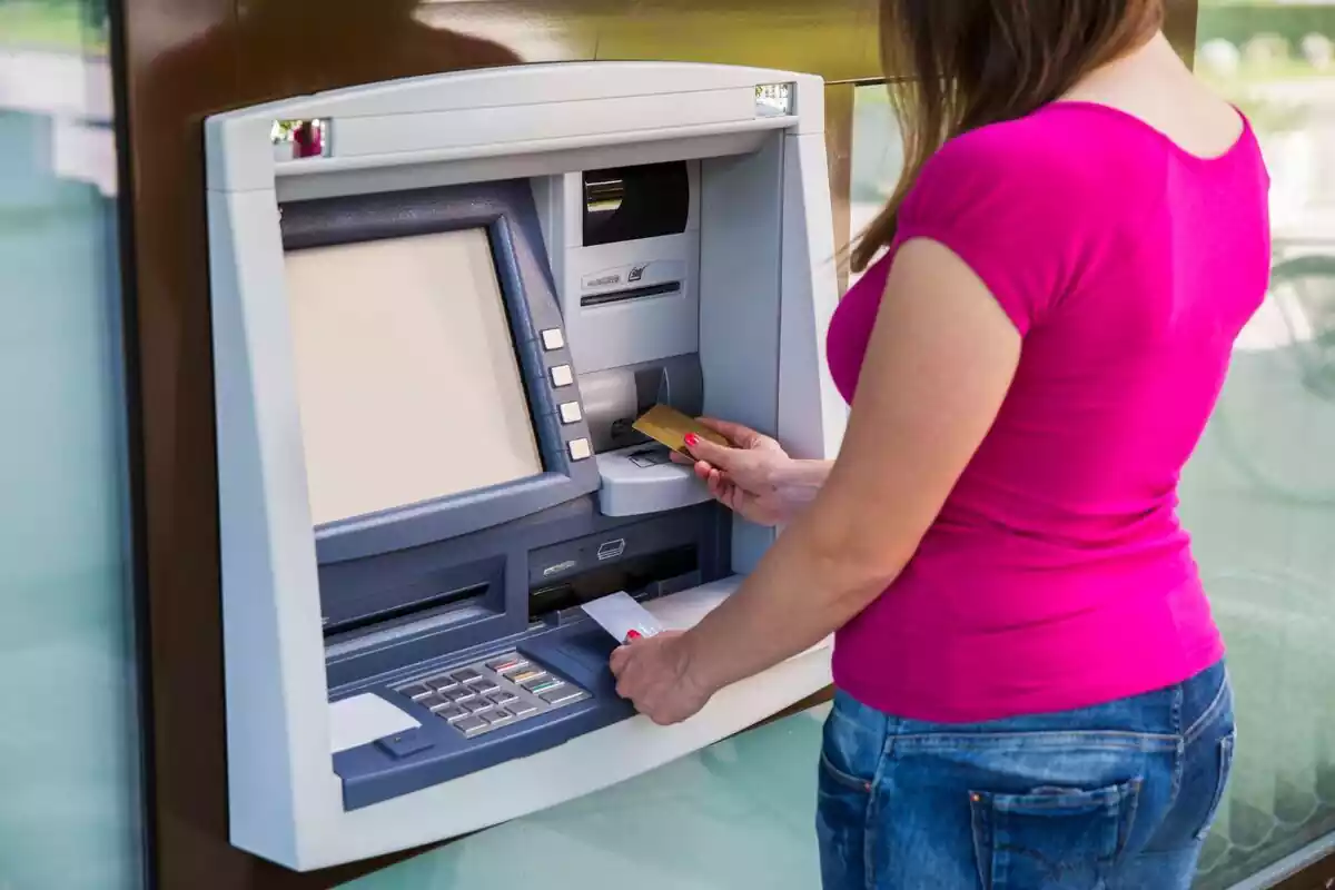 Una mujer introduciendo su tarjeta bancaria en un cajero automático con la pantalla en blanco