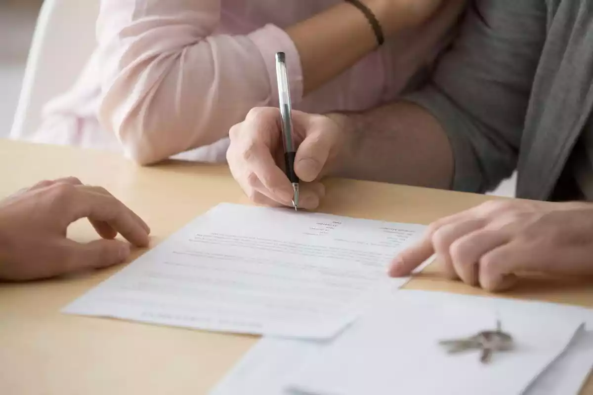 Una persona firmando un documento con un bolígrafo junto a su pareja