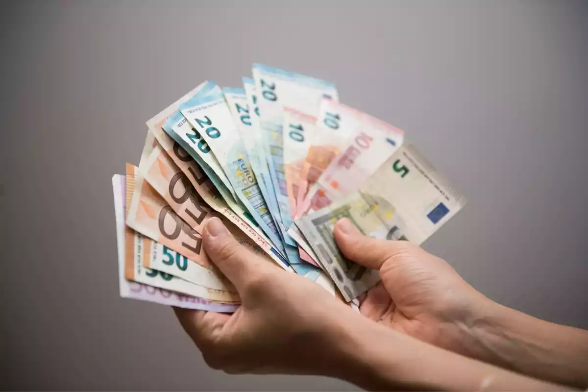 Imagen de unas manos agarrando billetes de euro en forma de abanico