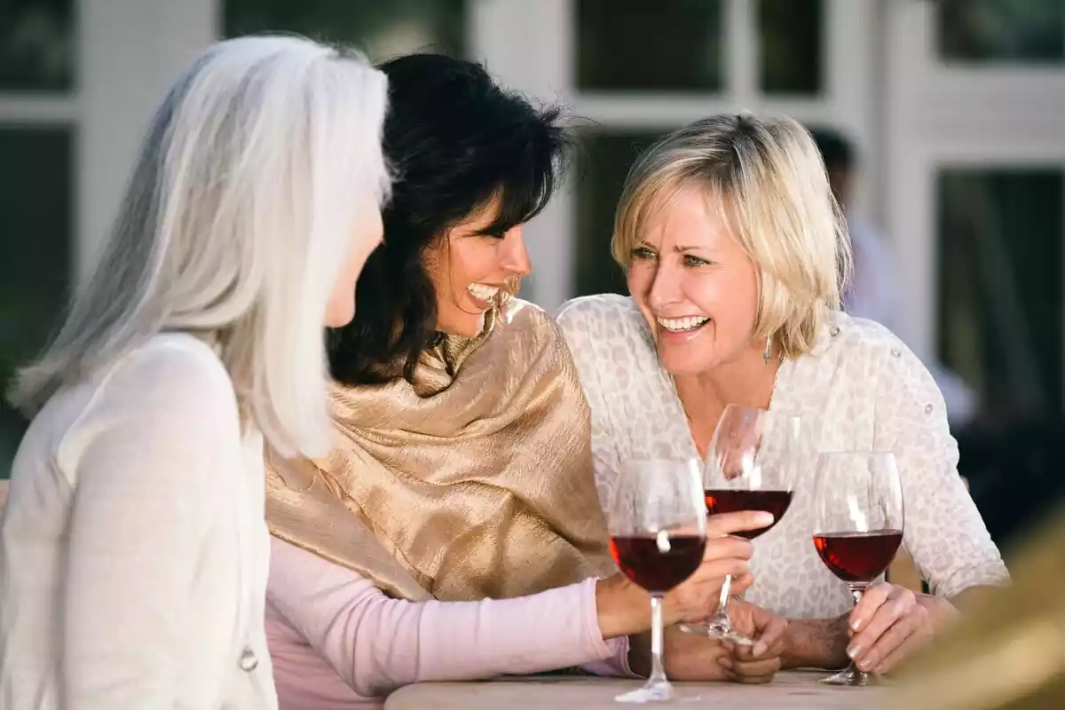 Grupo de tres mujeres bebiendo vino y riendo
