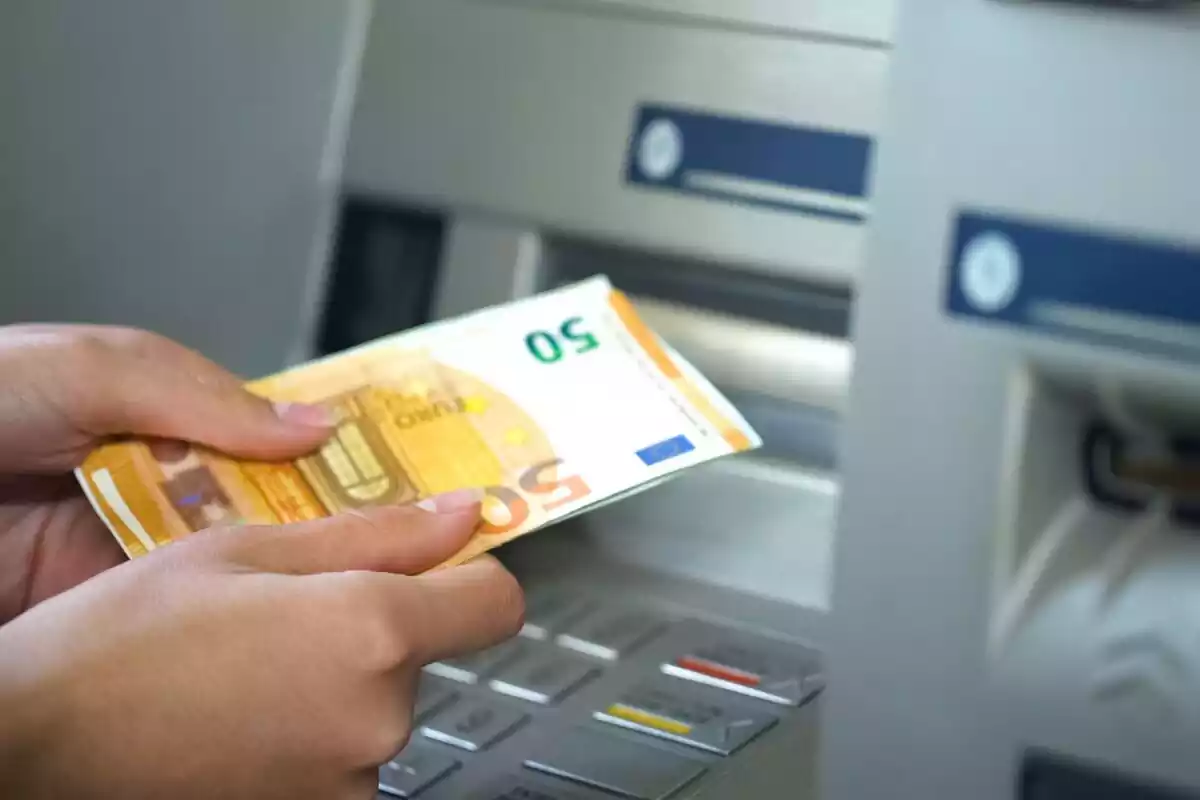 Dos manos sujetando billetes de 50 euros delante de un cajero