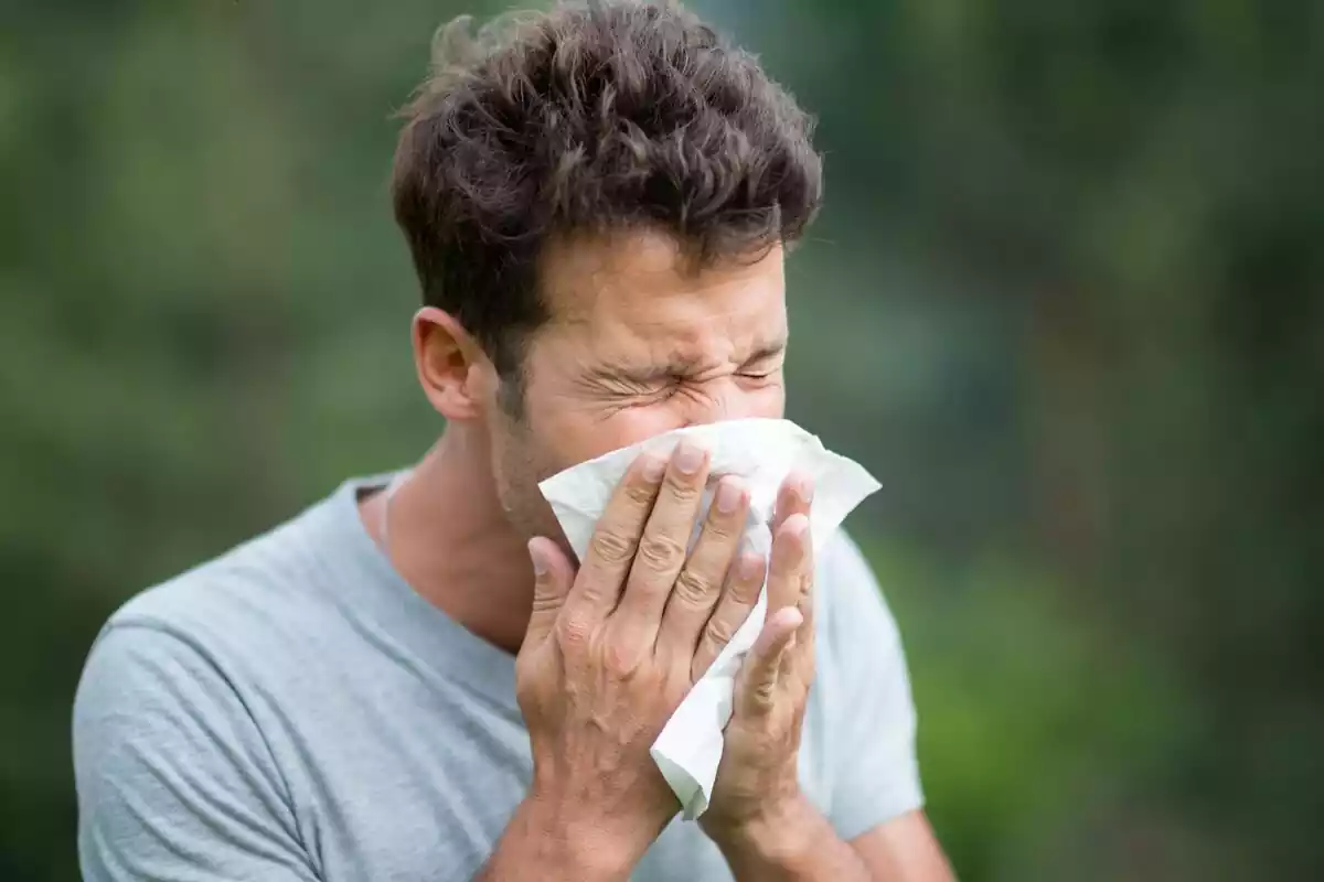 Hombre estornudando y tapándose con un pañuelo la nariz