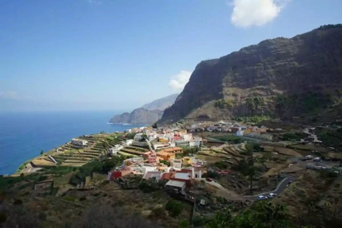 Vista panorámica de un pueblo costero con terrazas agrícolas y montañas al fondo.