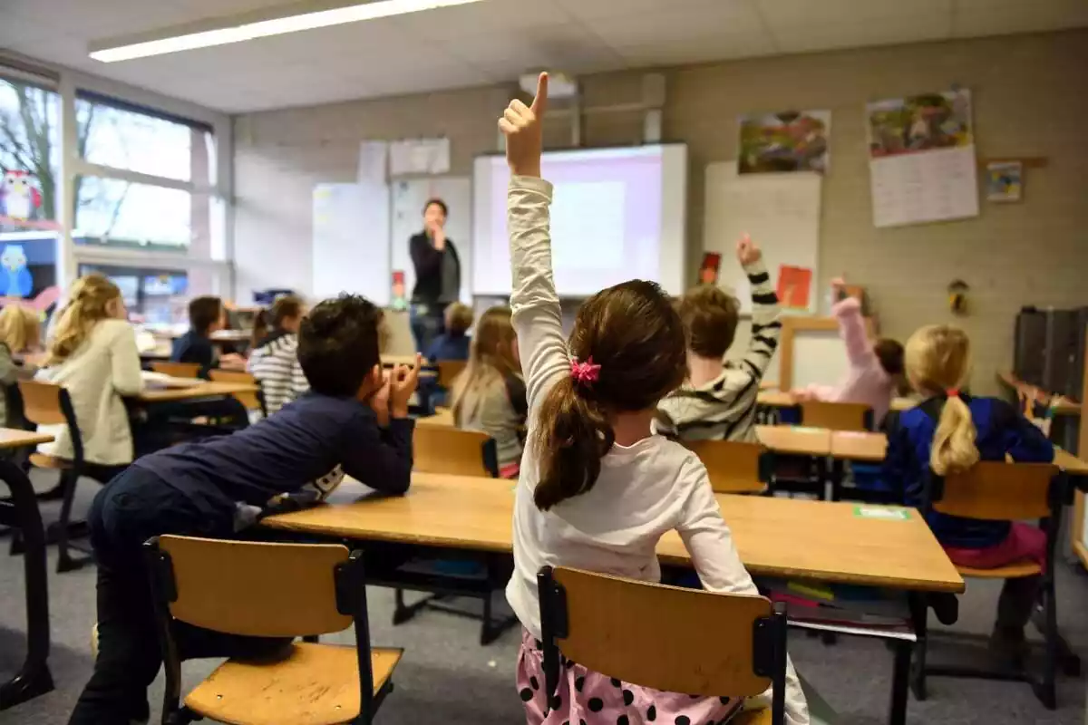 Aula de un colegio con alumnos de primaria levantando el brazo