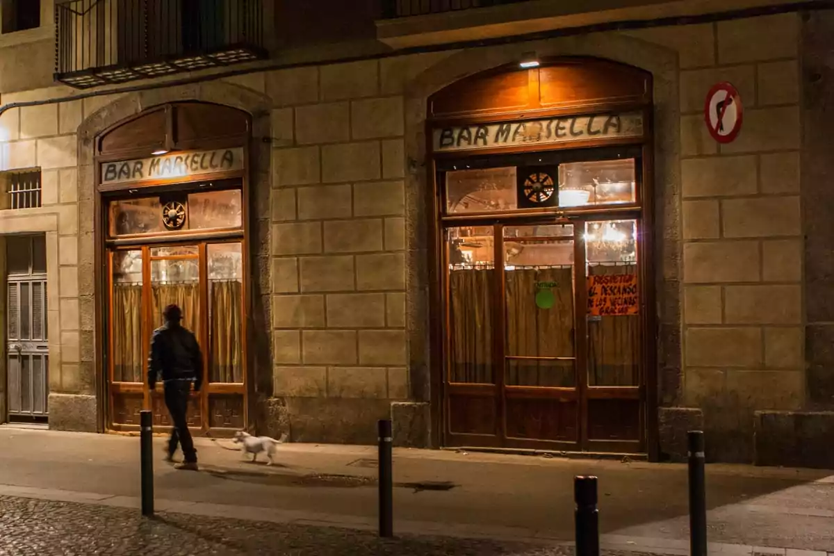 Una persona pasea a un perro frente a un bar llamado 