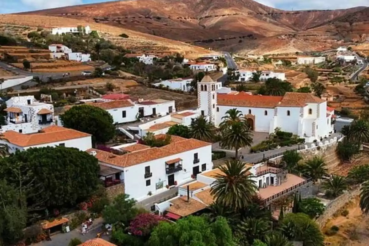 Vista aérea de un pintoresco pueblo con casas blancas y techos de tejas rojas, rodeado de colinas áridas y vegetación.