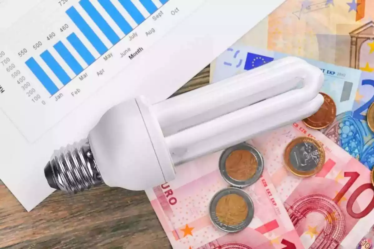 Una bombilla encima de una factura de la luz junto a billetes y monedas de euro