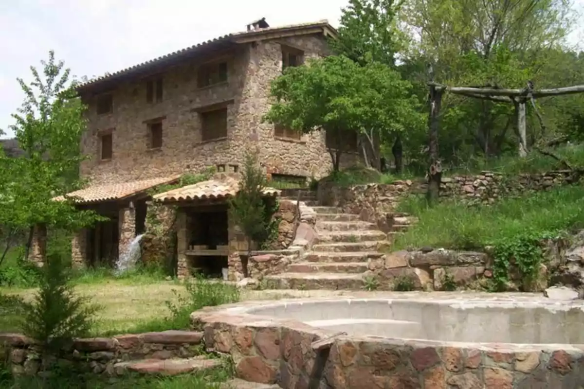 Casa de campo de piedra con escaleras y árboles alrededor.