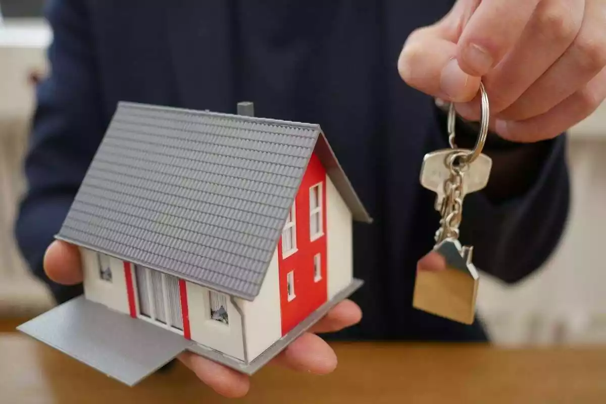 Una persona enseñando la maqueta de una casa en miniatura y unas llaves