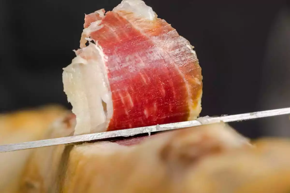 Primer plano de un corte de jamón serrano con un cuchillo alargado y afilado