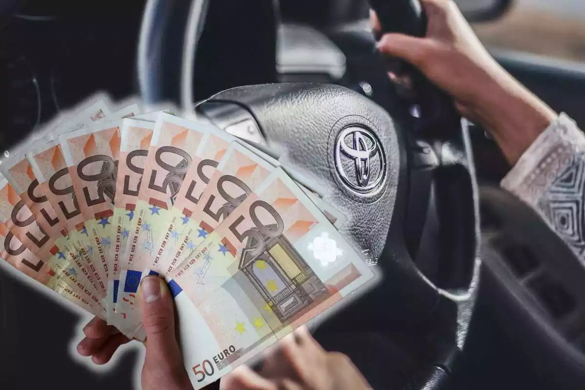 Una mano sujetando varios billetes de 50 euros y de fondo una persona con el volante de un coche