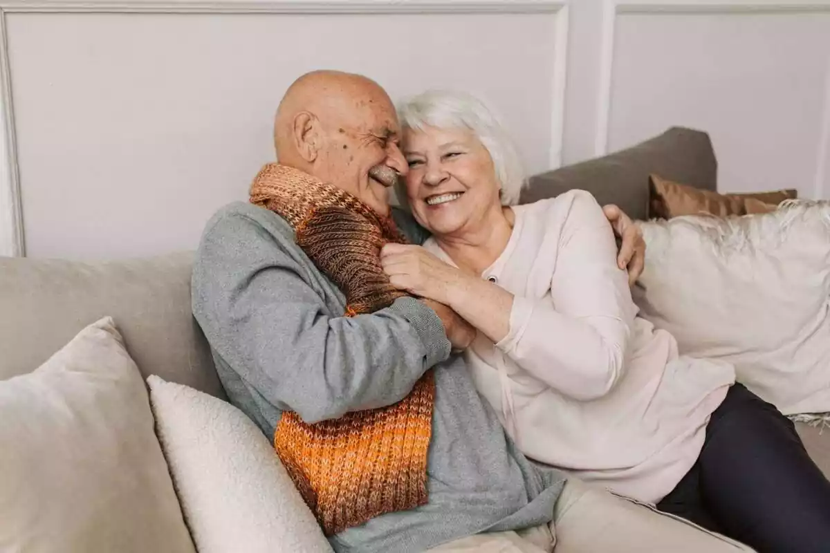 Dos personas mayores riendo sentadas en un sofá