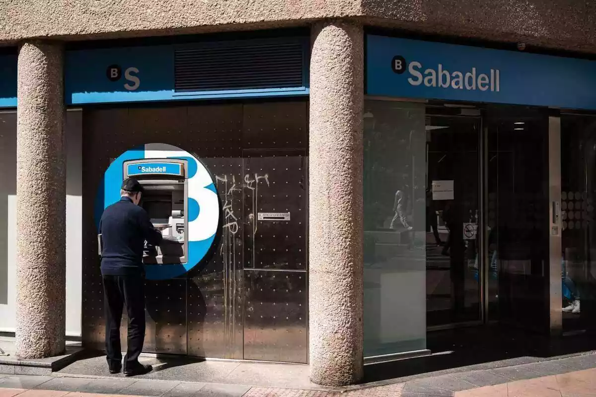 Anciano utilizando el cajero automático exterior del banco Sabadell
