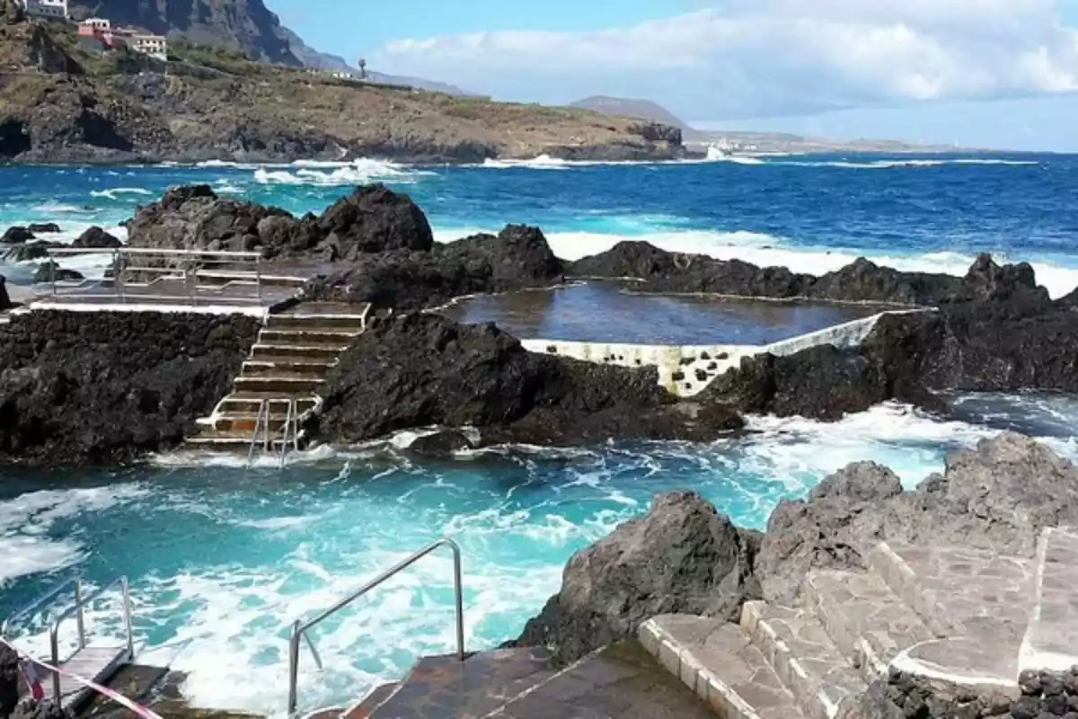 Una piscina natural rodeada de rocas volcánicas con escaleras de acceso y el mar de fondo.