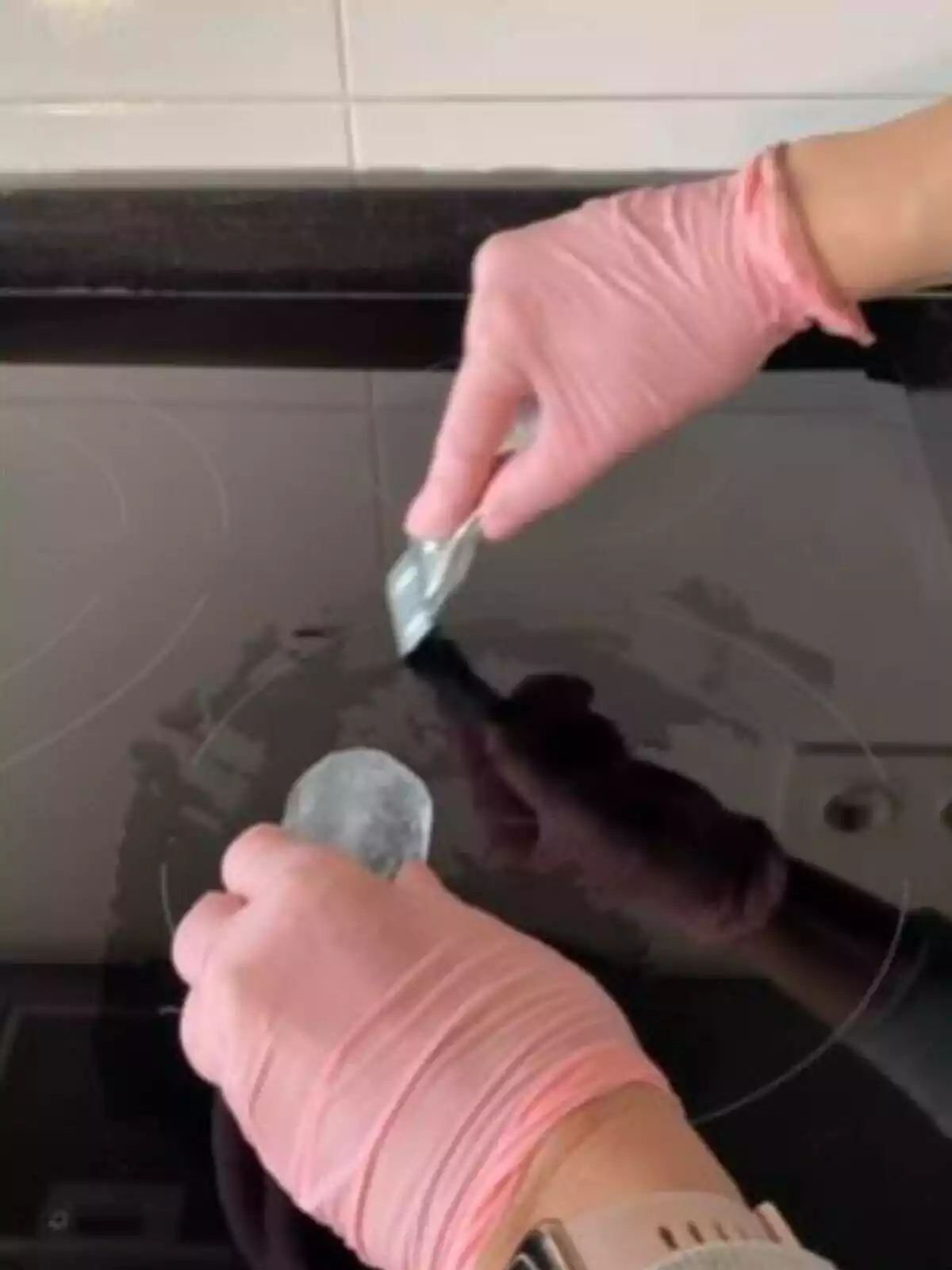 Imagen de las manos de una persona con guantes pasando un hielo por una vitrocerámica y una rascadora
