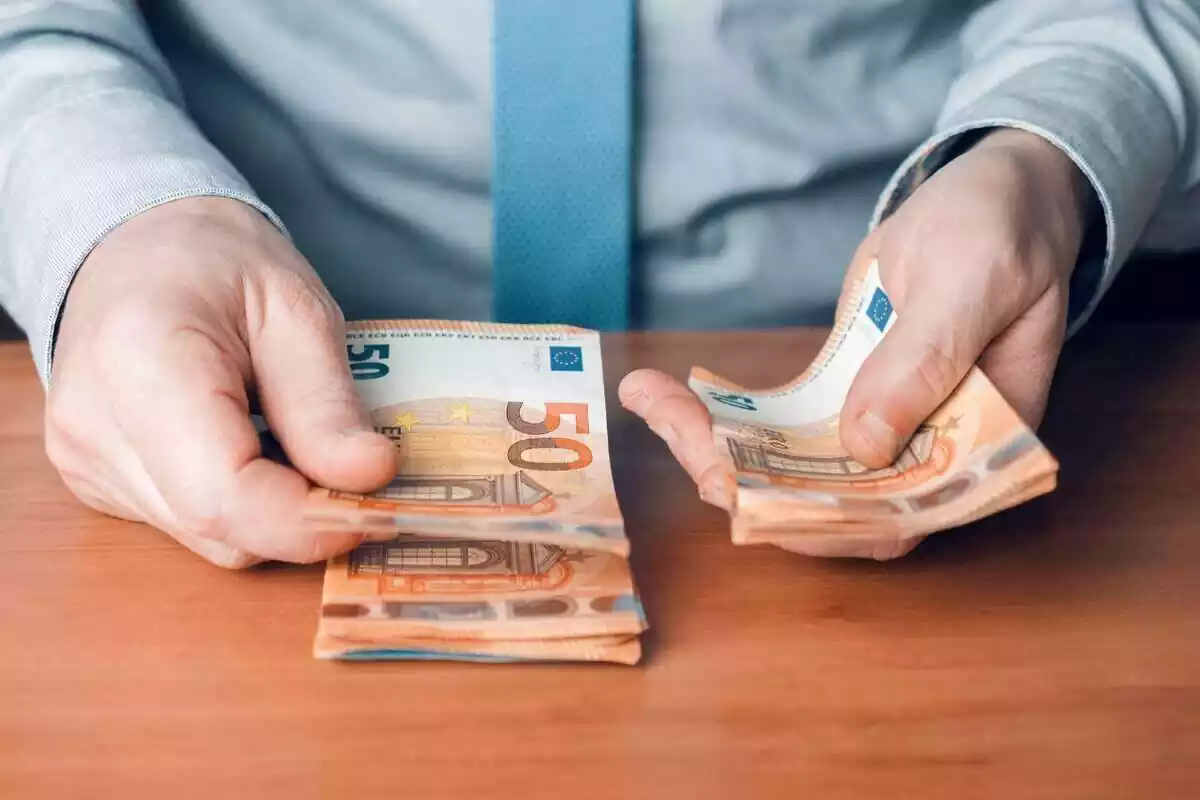 Manos de un hombre con camisa y corbata azul, contando billetes de 50 euros
