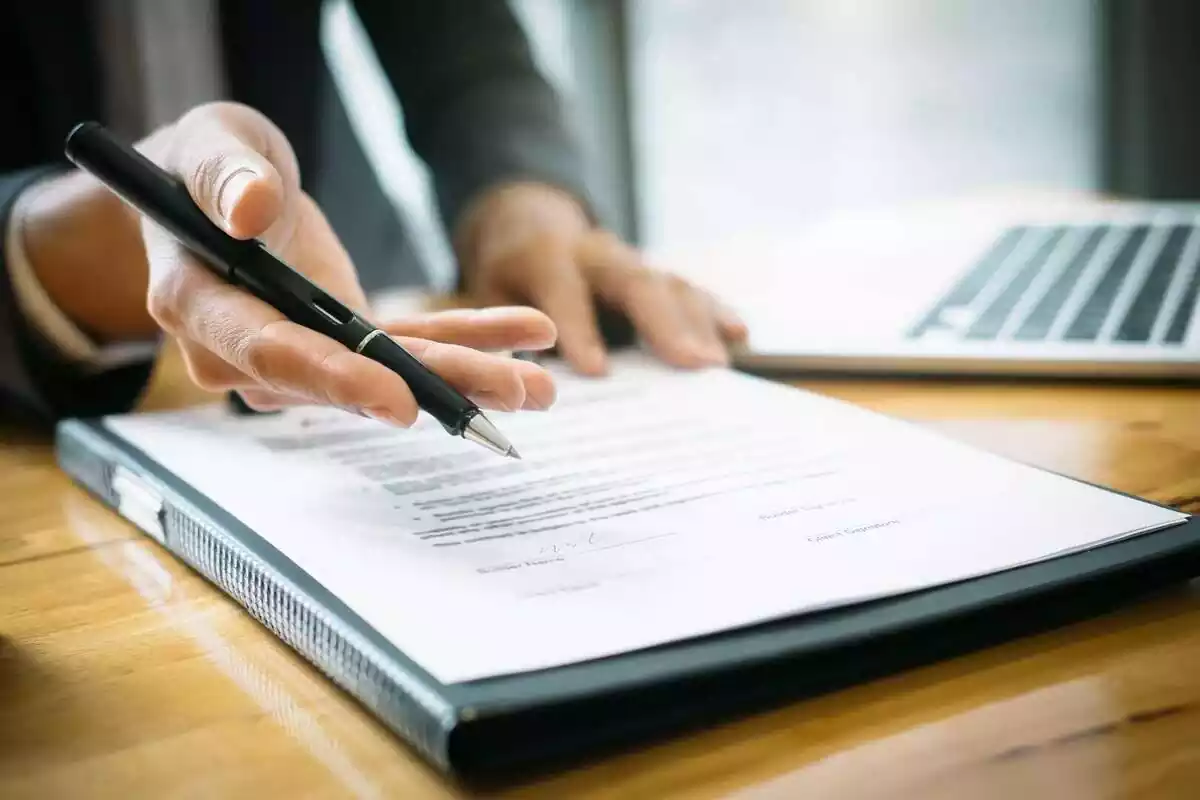 Hombre tendiendo la mano con un bolígrafo para firmar un documento