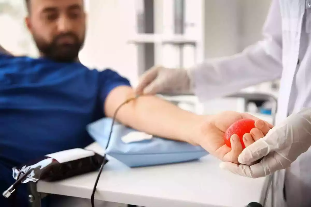 Hombre sentado en una camilla donando sangre con el brazo extendido y una pelota en la mano