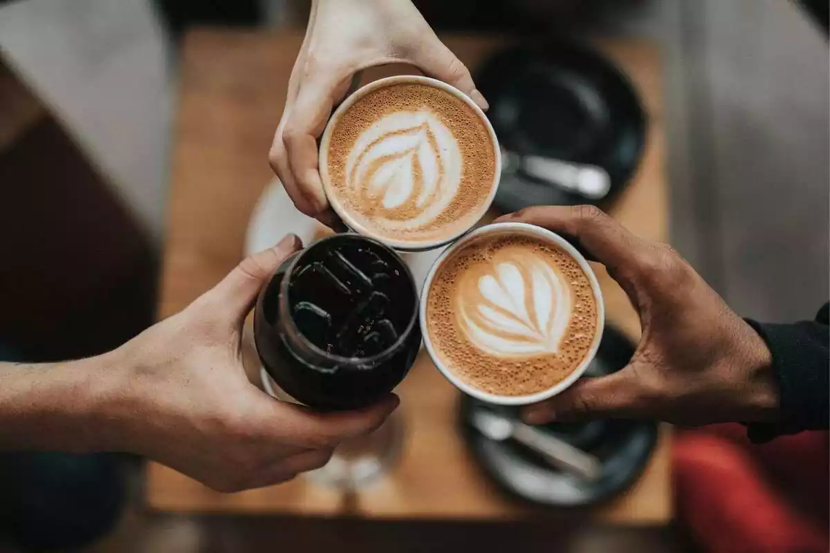 Imagen de tres cafés sujetados por tres personas y hecha desde arriba
