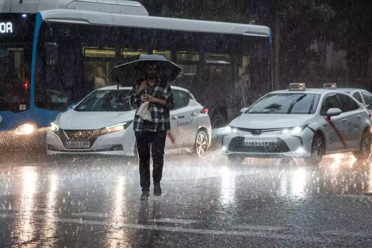 Un hombre atravesando la calle en medio de una tormenta y con coches detrás